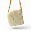 Panetto avorio di Piccoli Semi, shampoo solido artigianale appeso alla rafia, su sfondo bianco.